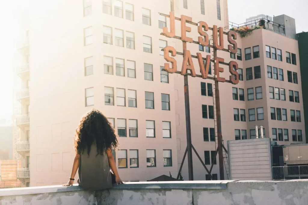 a woman, thinking about giving, sitting next to a sign that says "Jesus Saves"