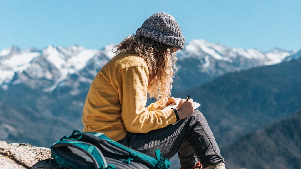 woman sitting on moutain writing in journal