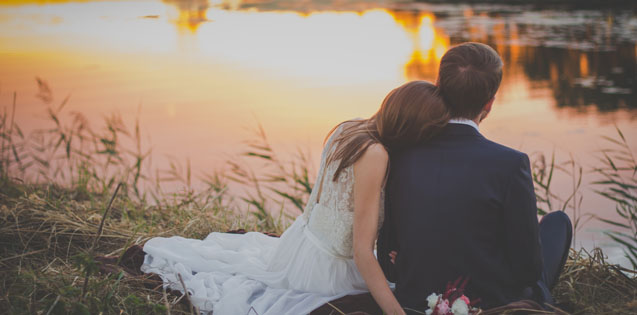 married couple sitting on lake shore