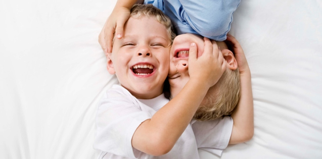two small boys laying on a bed playing with each other
