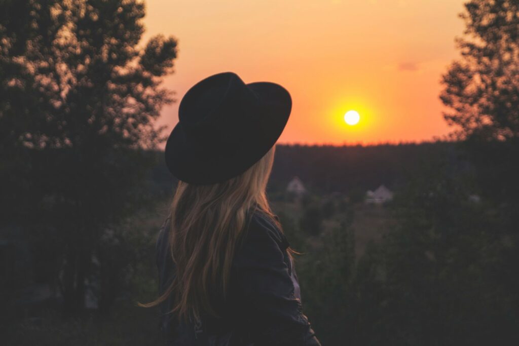 a woman wearing a black hat looking at a sunset, finding contentment in her singleness