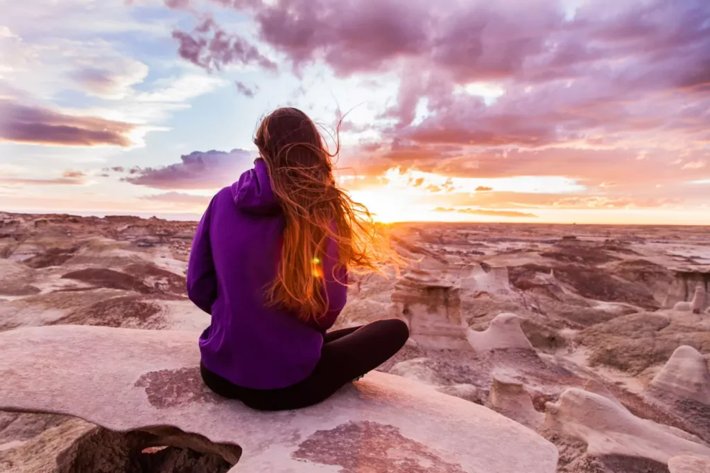 a woman sitting in a desert at sunset, worshipping El Roi - the God who sees